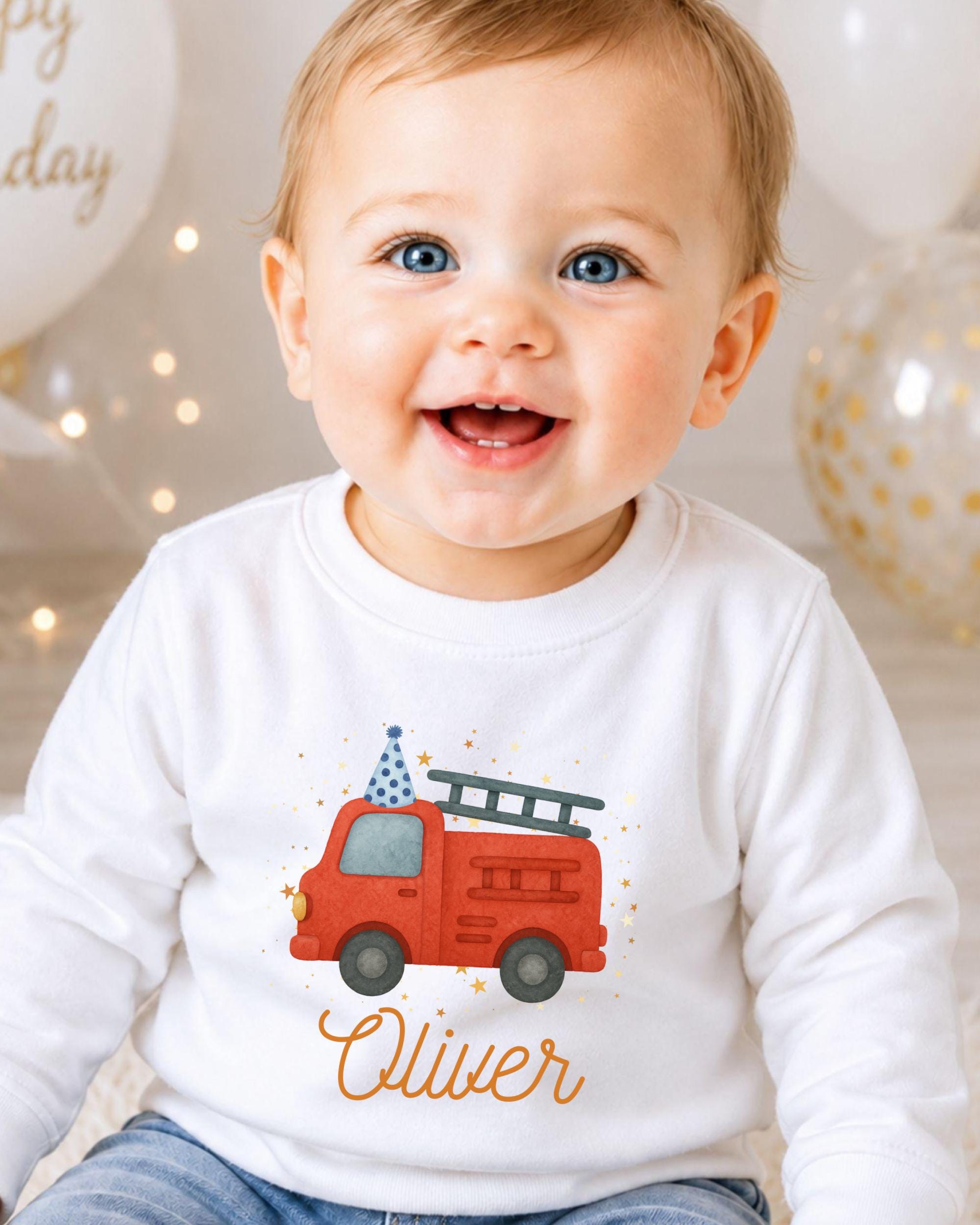 A smiling baby boy wearing a white shirt with a red fire truck graphic and the name "Olivier" printed on it.