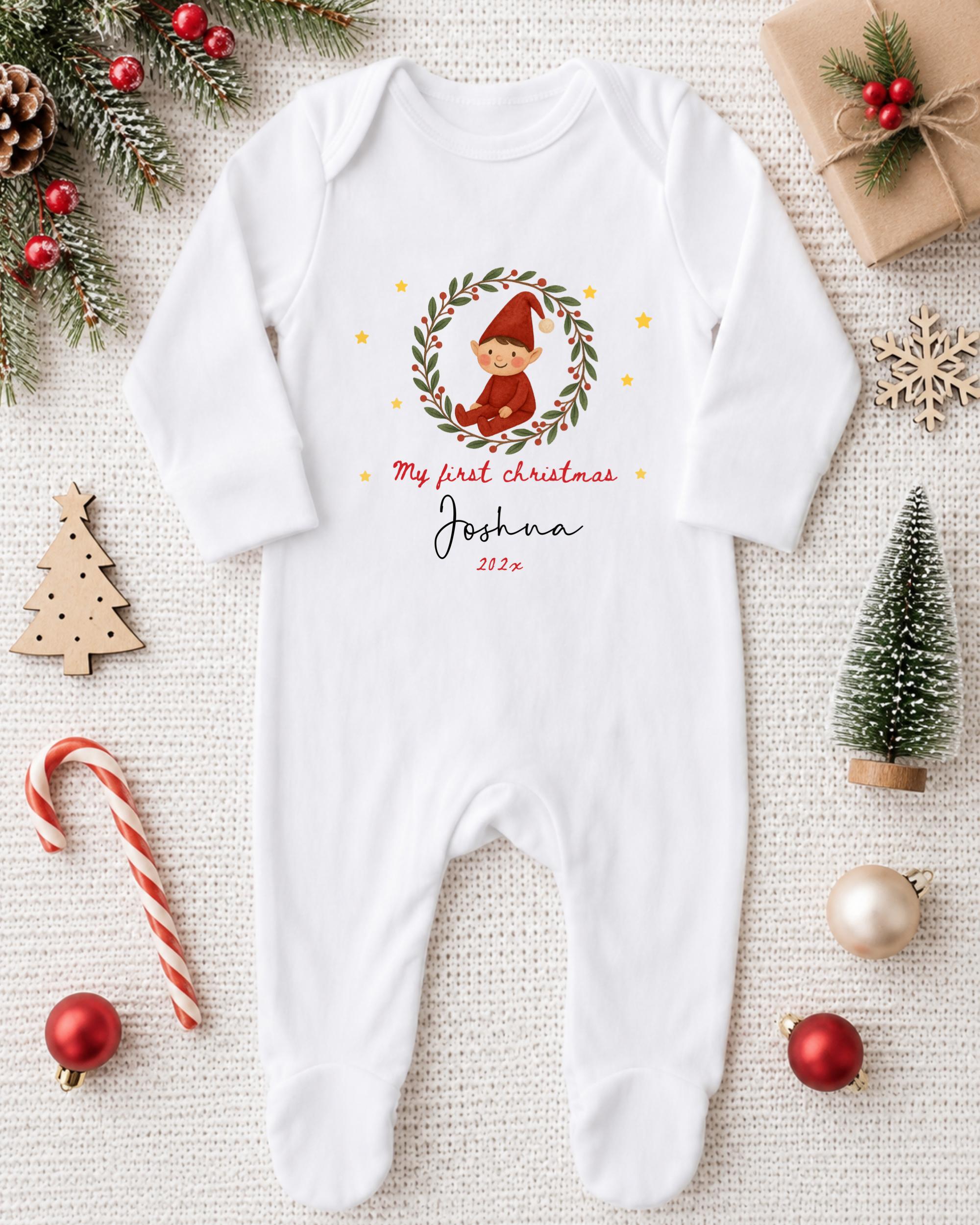 A white onesie with a Christmas-themed design, featuring a small elf or gnome, is displayed on a white background alongside various Christmas decorations and ornaments.