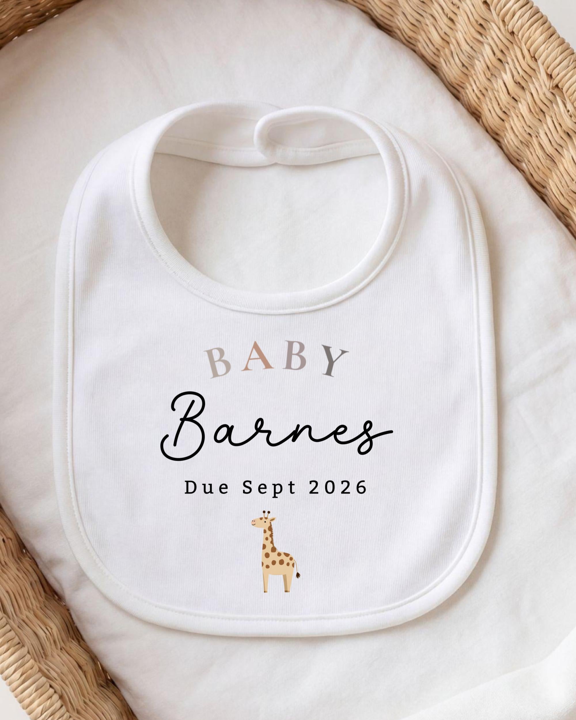 A white baby bib with the text "BABY Barnes Due Sept 2026" printed on it, along with a small giraffe illustration.