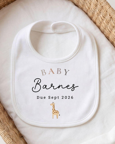 A white baby bib with the text "BABY Barnes Due Sept 2026" printed on it, along with a small giraffe illustration.