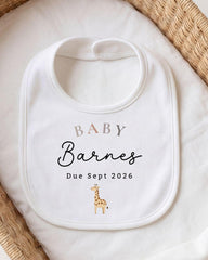A white baby bib with the text "BABY Barnes Due Sept 2026" printed on it, along with a small giraffe illustration.