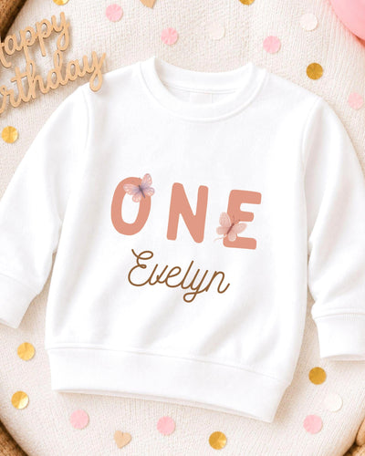 A white sweatshirt with the text "ONE Evelyn" printed on it, surrounded by confetti.