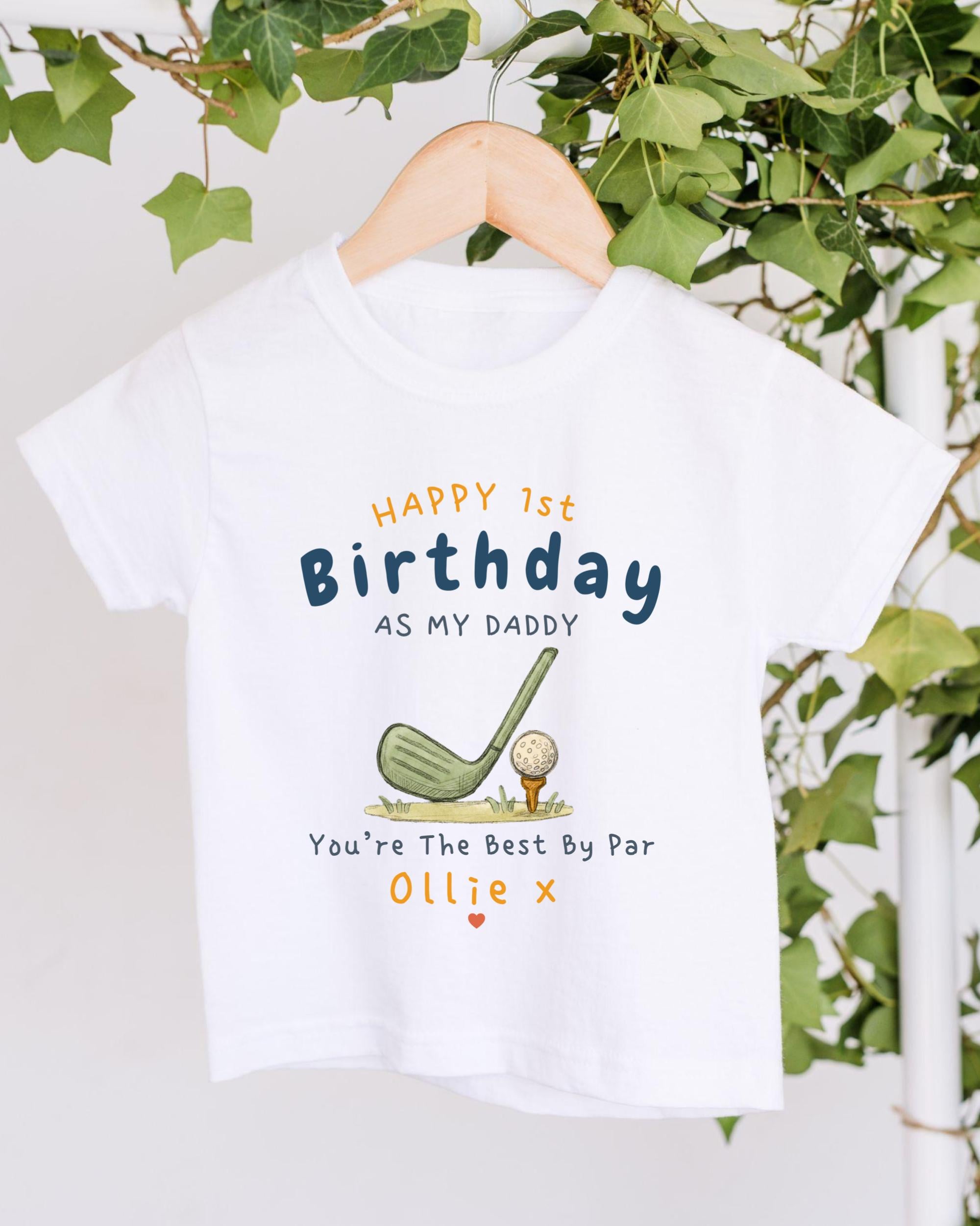 A white t-shirt with a golf-themed design and text printed on it, hanging on a wooden hanger.