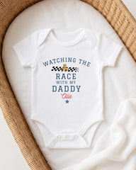 A white onesie with a racing theme and text printed on it, placed in a woven basket.