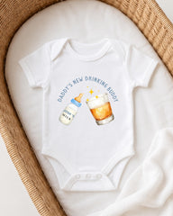 A white onesie with a humorous text and illustrations on it, placed on a white blanket.