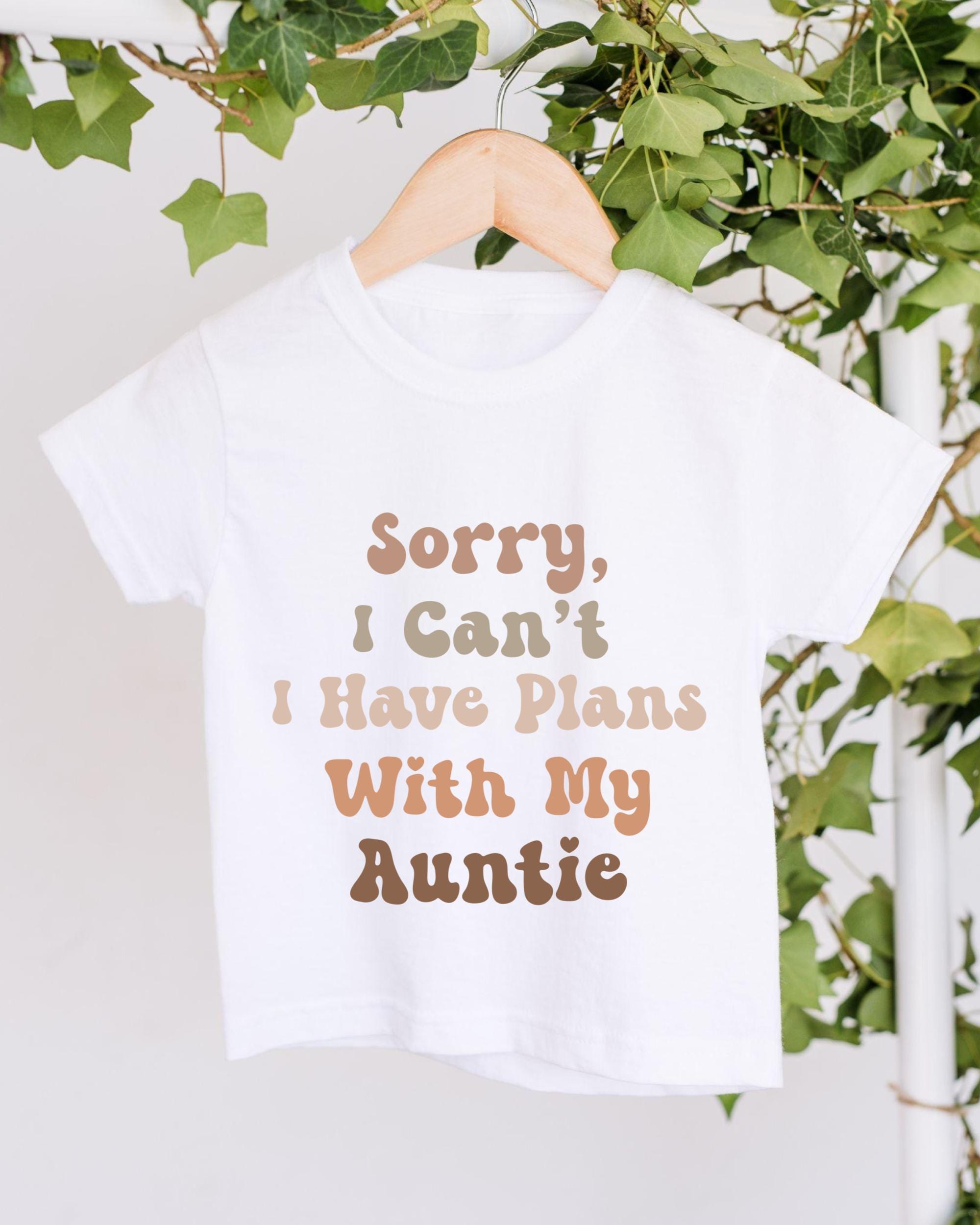 A white t-shirt with text printed on it, hanging on a wooden hanger.