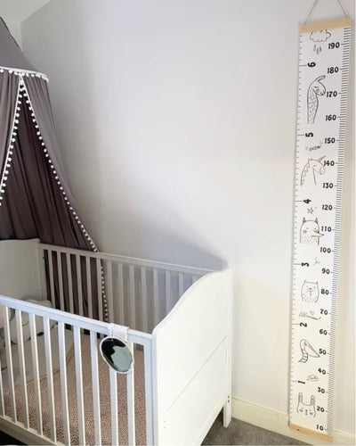 a white crib next to a white wall with a large ruler on it