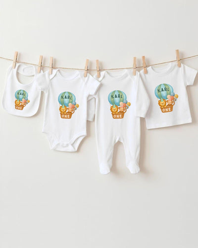 A collection of baby clothes, including bodysuits and bibs, hanging on a clothesline.