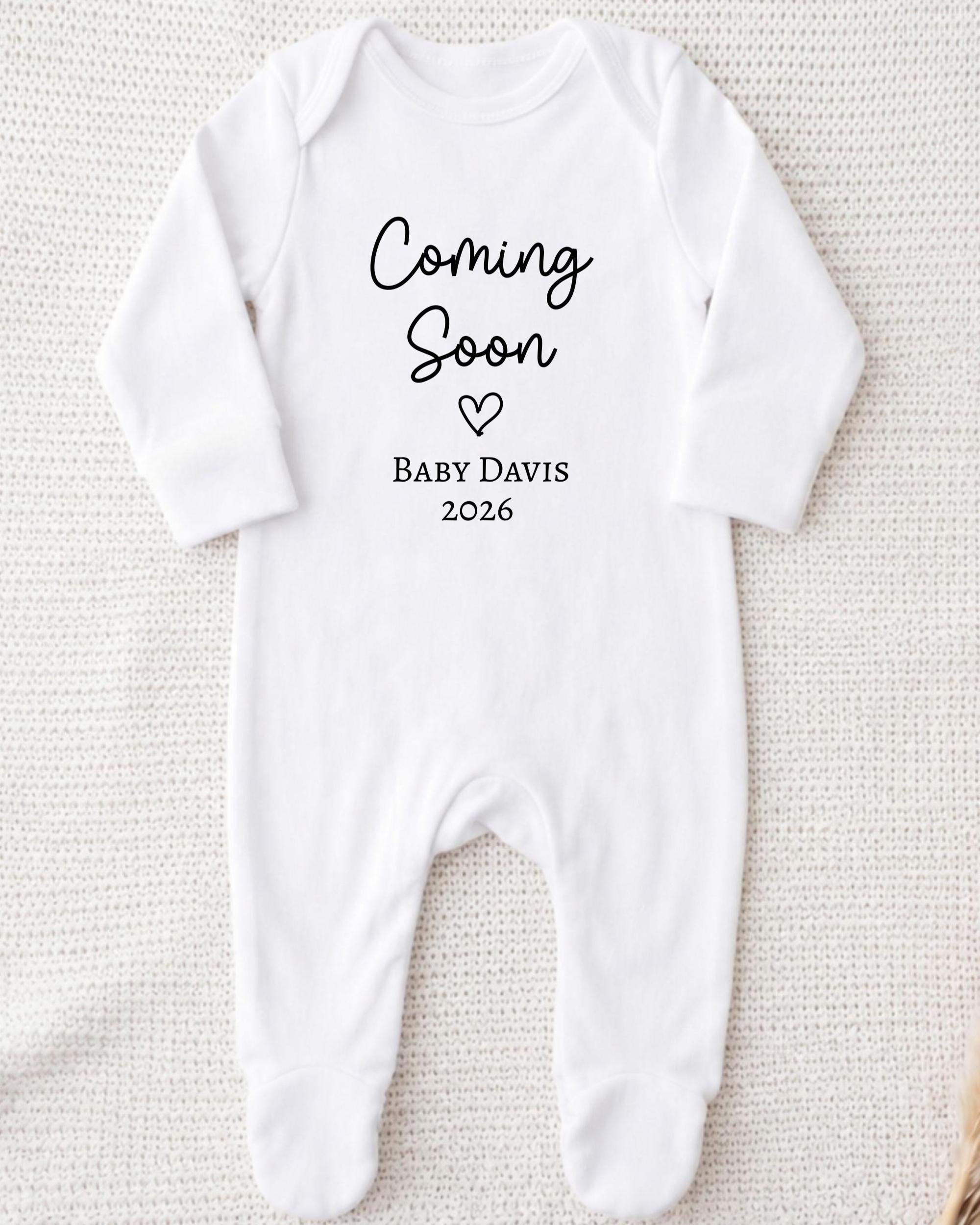 A white onesie with the text "Coming Soon Baby Davis 2026" printed on it.