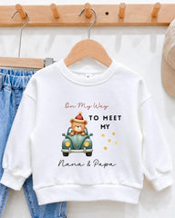 A white sweatshirt with a cartoon image of a bear in a car and text that says "On My Way to Meet My Nana & Papa".