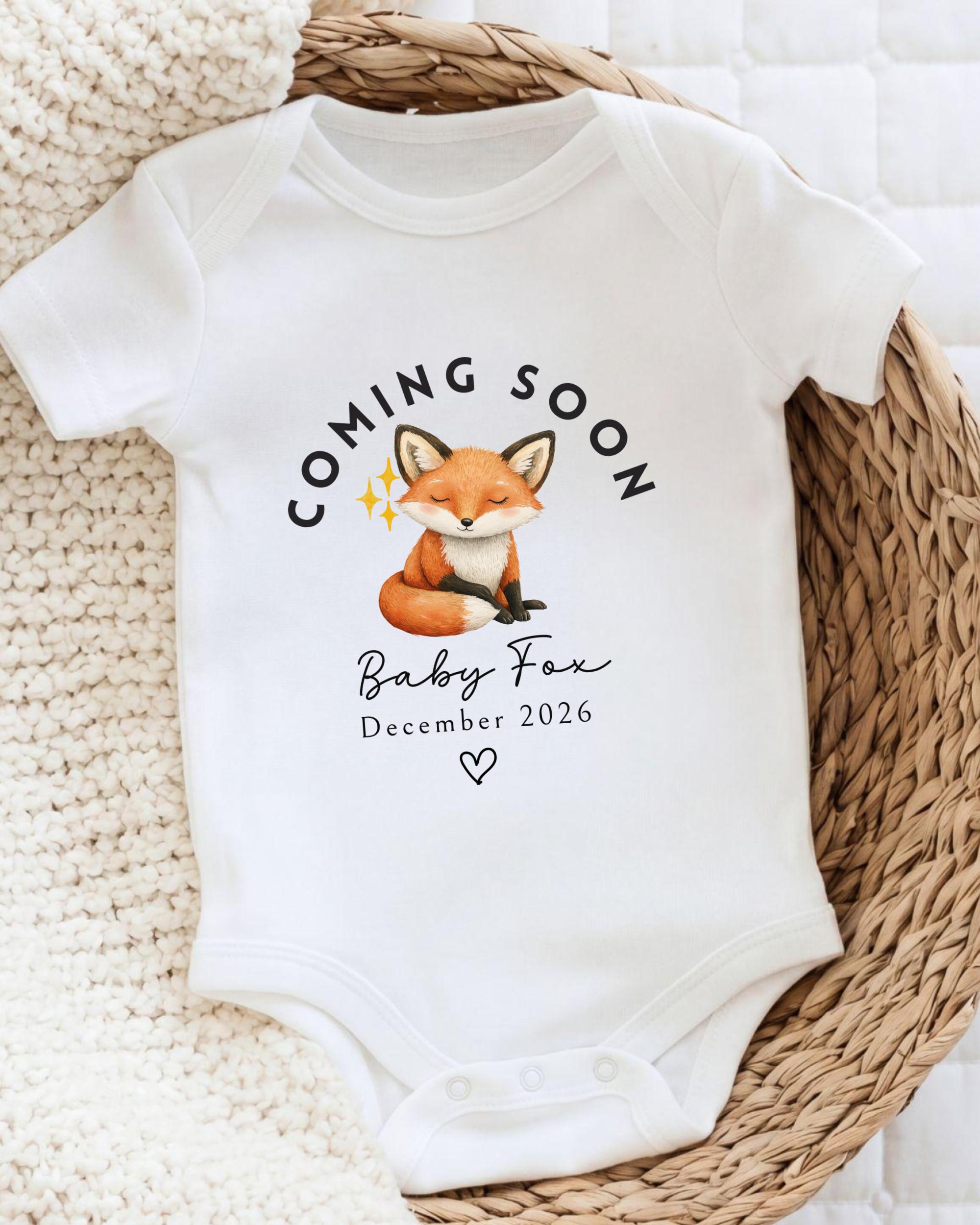 A white baby onesie with a graphic of a fox and the text "Coming soon Baby Fox December 2026" printed on it.