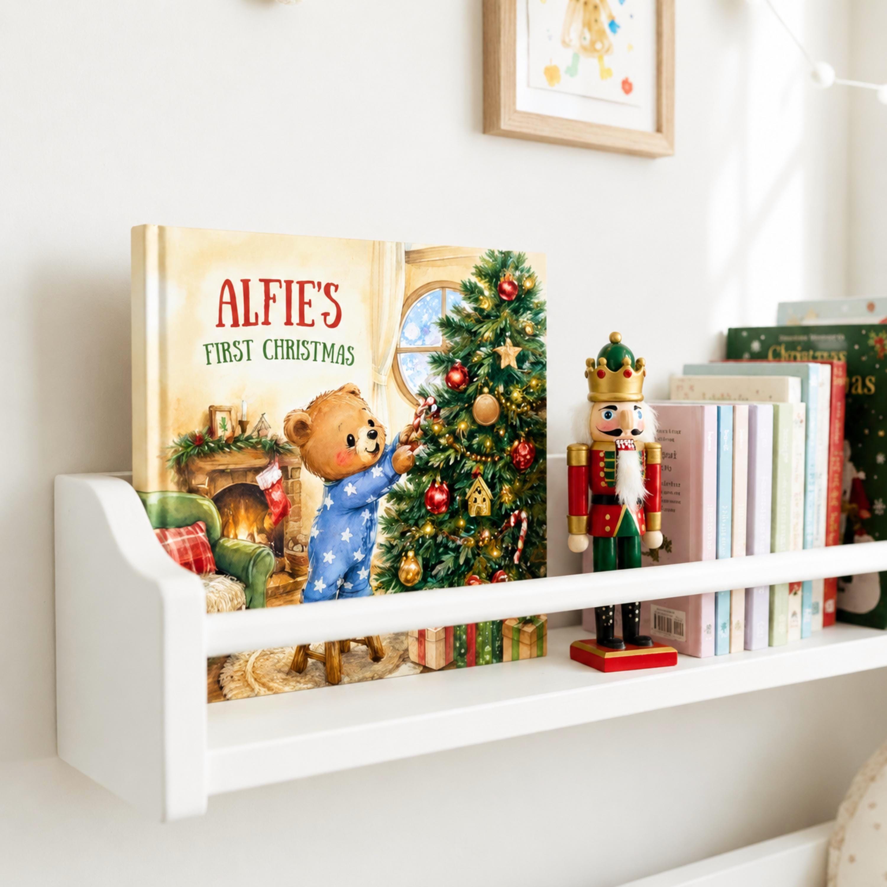 A white bookshelf displaying a children's book titled "Alfie's First Christmas" and a nutcracker figurine.