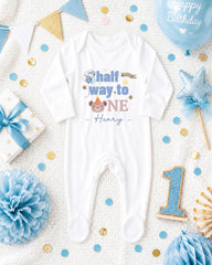 A white onesie with the text "half way to one" printed on it, surrounded by birthday decorations such as a blue balloon, blue and gold confetti, and a blue and gold star.
