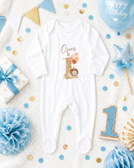 A white onesie with the name "Oscar" printed on it, surrounded by various baby-themed items such as a blue balloon, a blue and gold star, and blue and gold confetti.