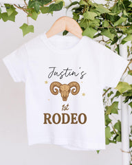 A white t-shirt with a graphic design and text printed on it, hanging on a wooden hanger.
