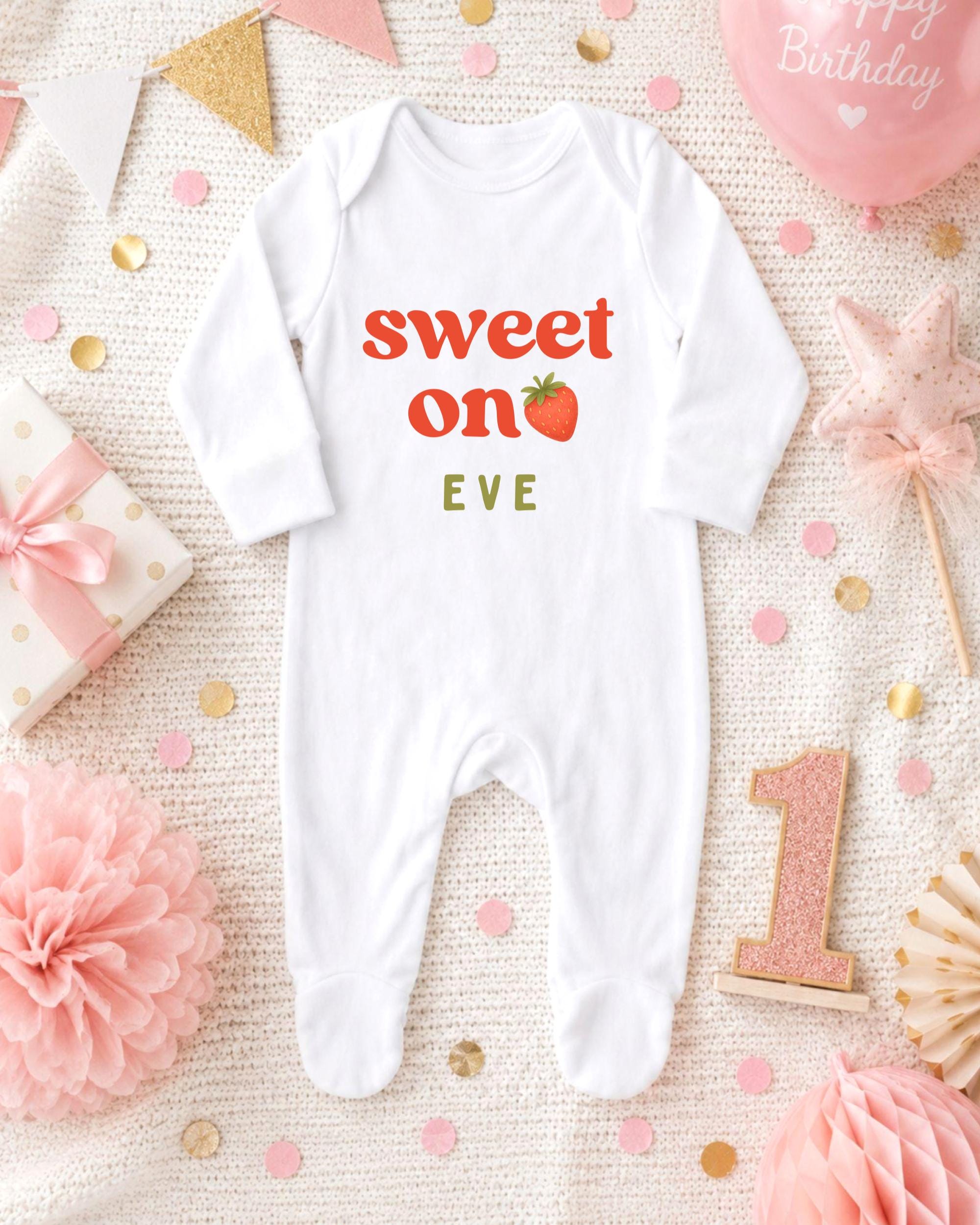 A white onesie with the text "Sweet on Eve" printed on it, surrounded by pink and gold confetti, a pink star, and a pink balloon.