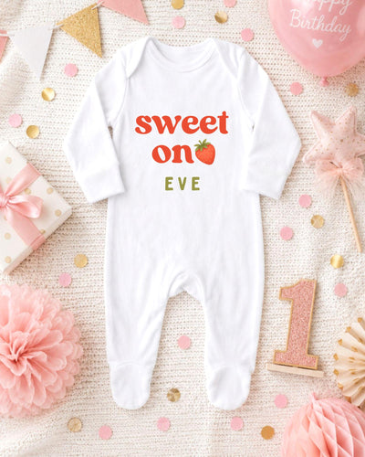 A white bodysuit with the text "Sweet on Eve" printed on it, surrounded by pink and gold confetti, a pink star, and a pink balloon.