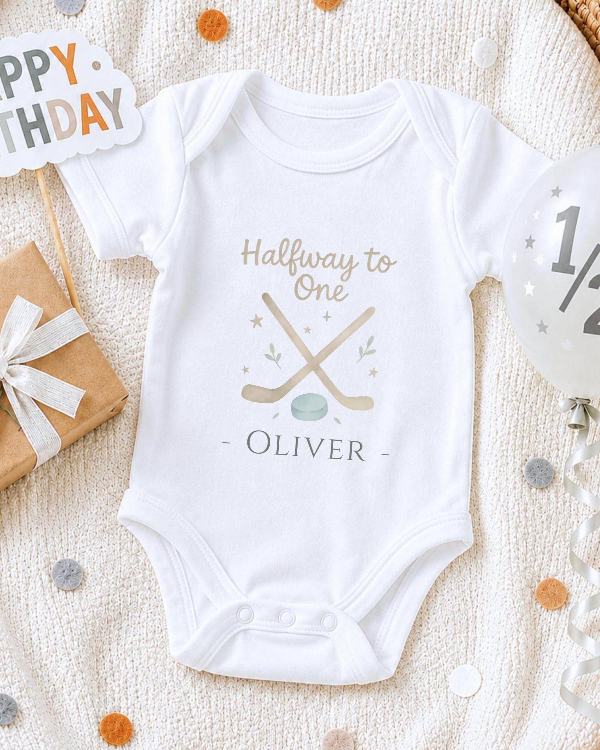 A white onesie with a personalized message printed on it, surrounded by confetti and a birthday sign.