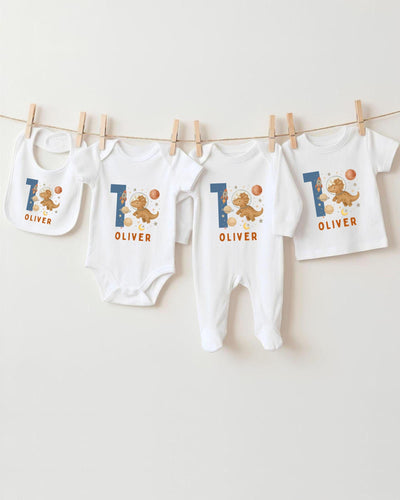 A collection of white baby clothes, including bodysuits and bibs, with the name "OLIVER" printed on them. The clothes are hanging on a clothesline, and there are four of them in total.