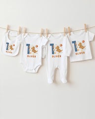 A collection of white baby clothes, including onesies and bibs, with the name "OLIVER" printed on them. The clothes are hanging on a clothesline, and there are four of them in total.