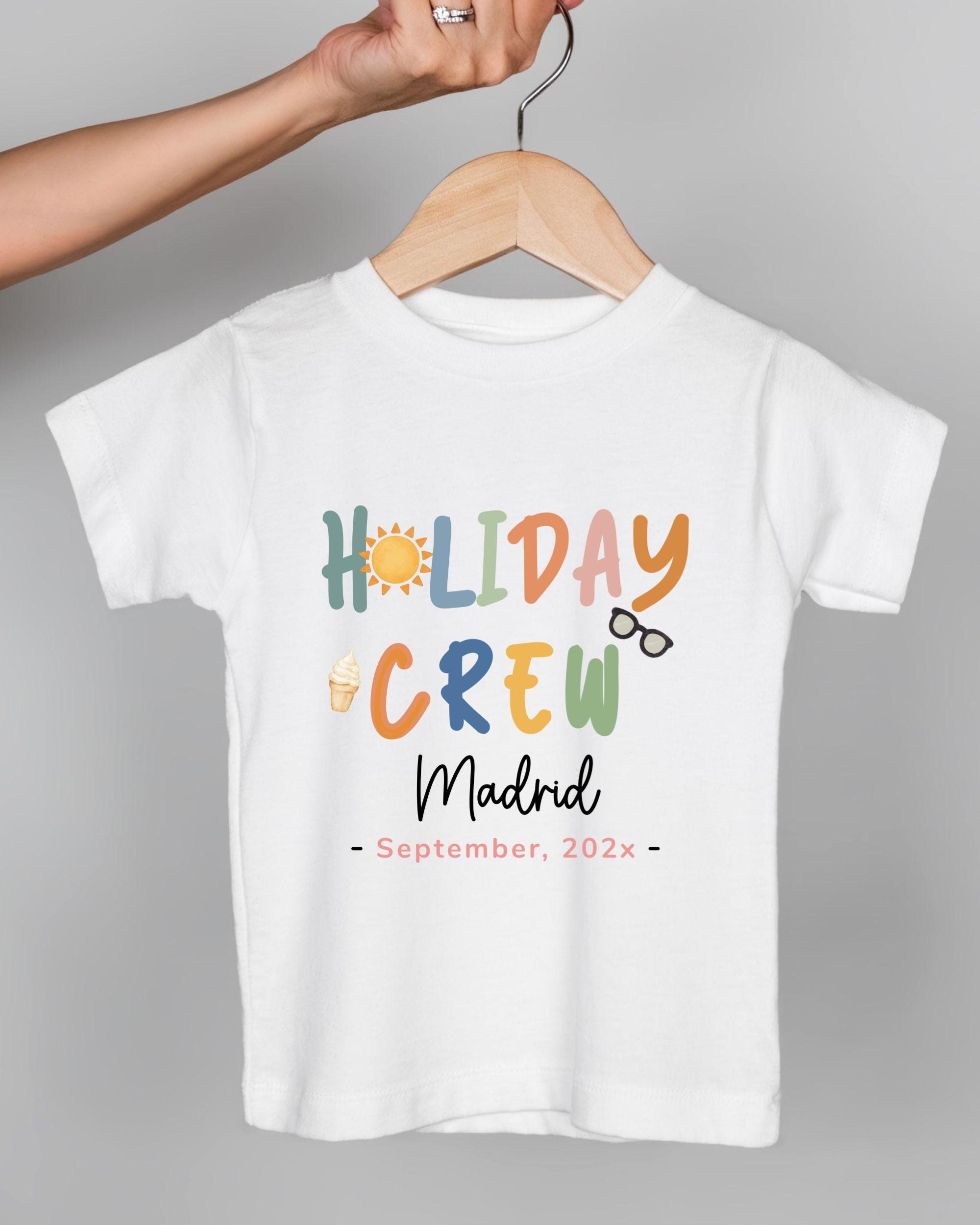A white t-shirt with colorful text and icons printed on it, hanging on a wooden hanger.