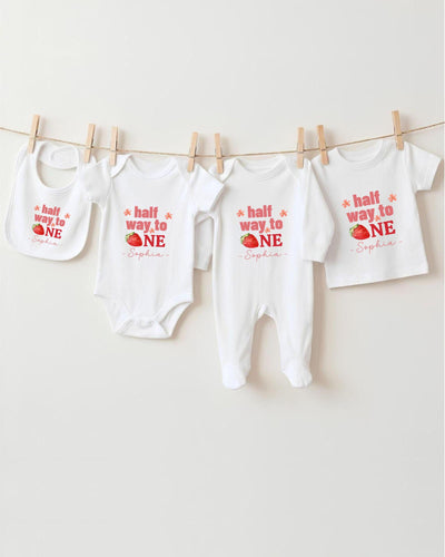 A row of white baby clothes with red text and images, including a bib and a t-shirt, hanging on a clothesline.