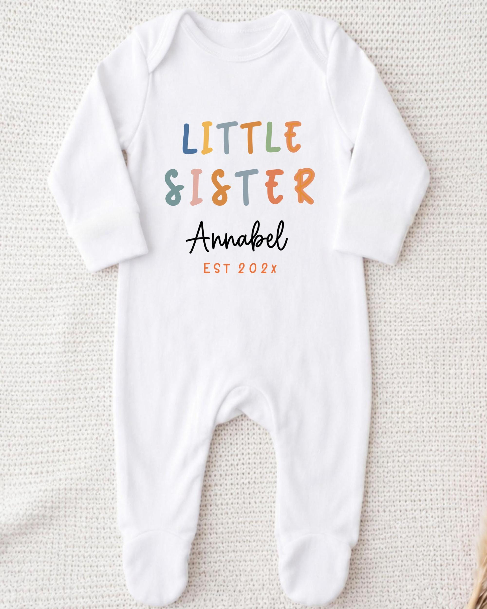 A white onesie with the text "Little Sister Annabel" printed on it.