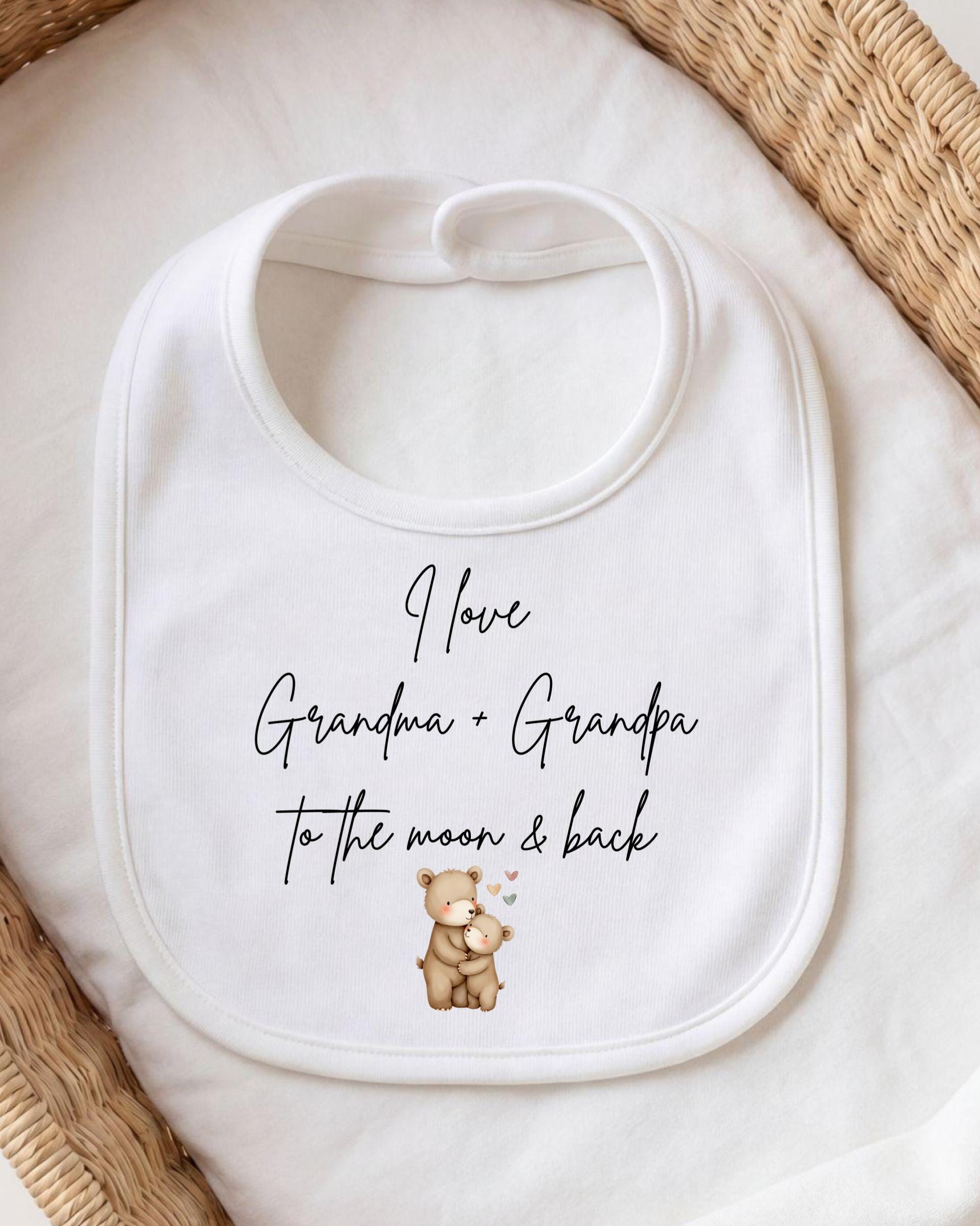 A white bib with a printed message that reads "I love Grandma + Grandpa to the moon & back" along with an illustration of a bear and a baby.