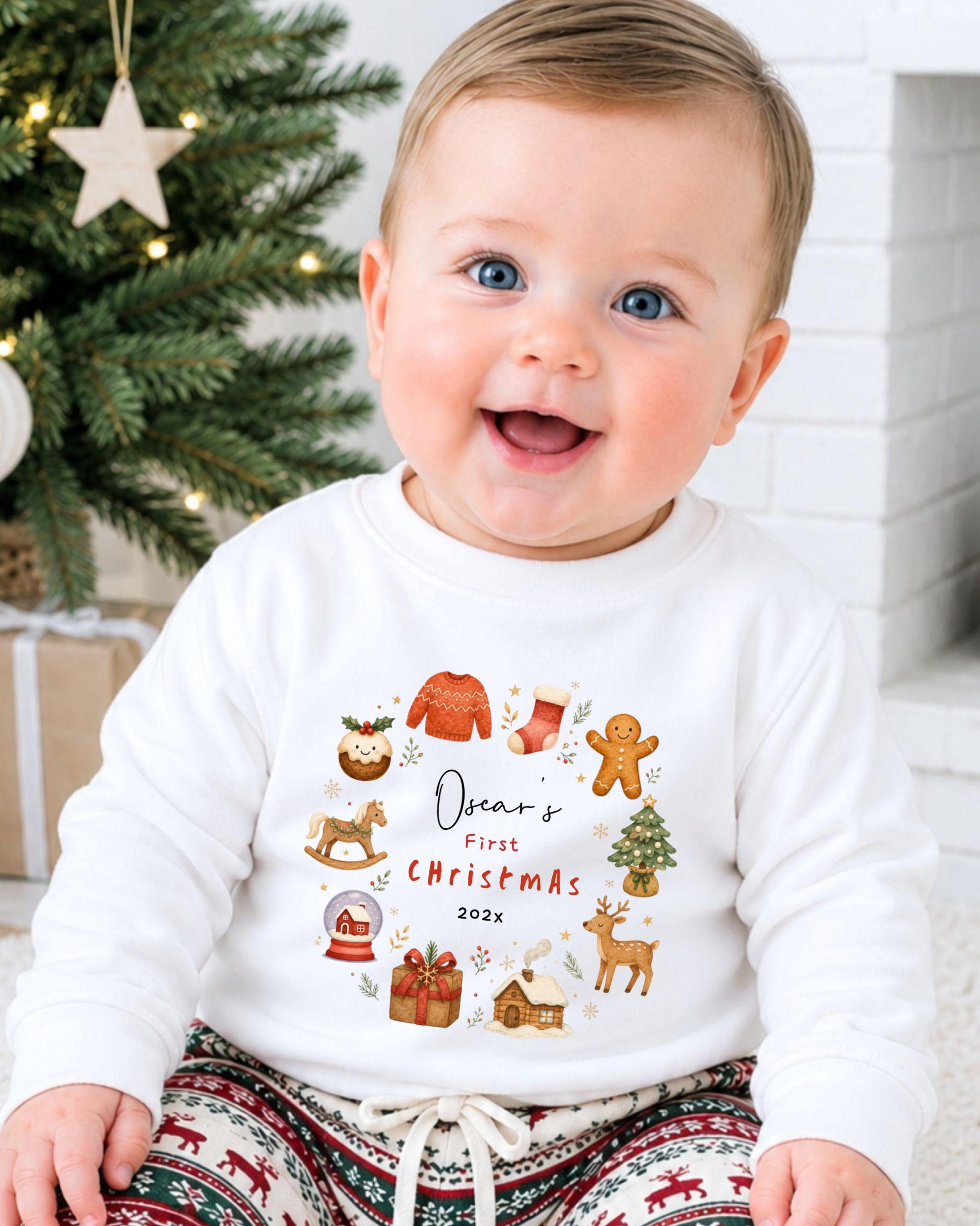 A smiling baby wearing a white sweater with a Christmas-themed design and text, sitting in front of a Christmas tree.