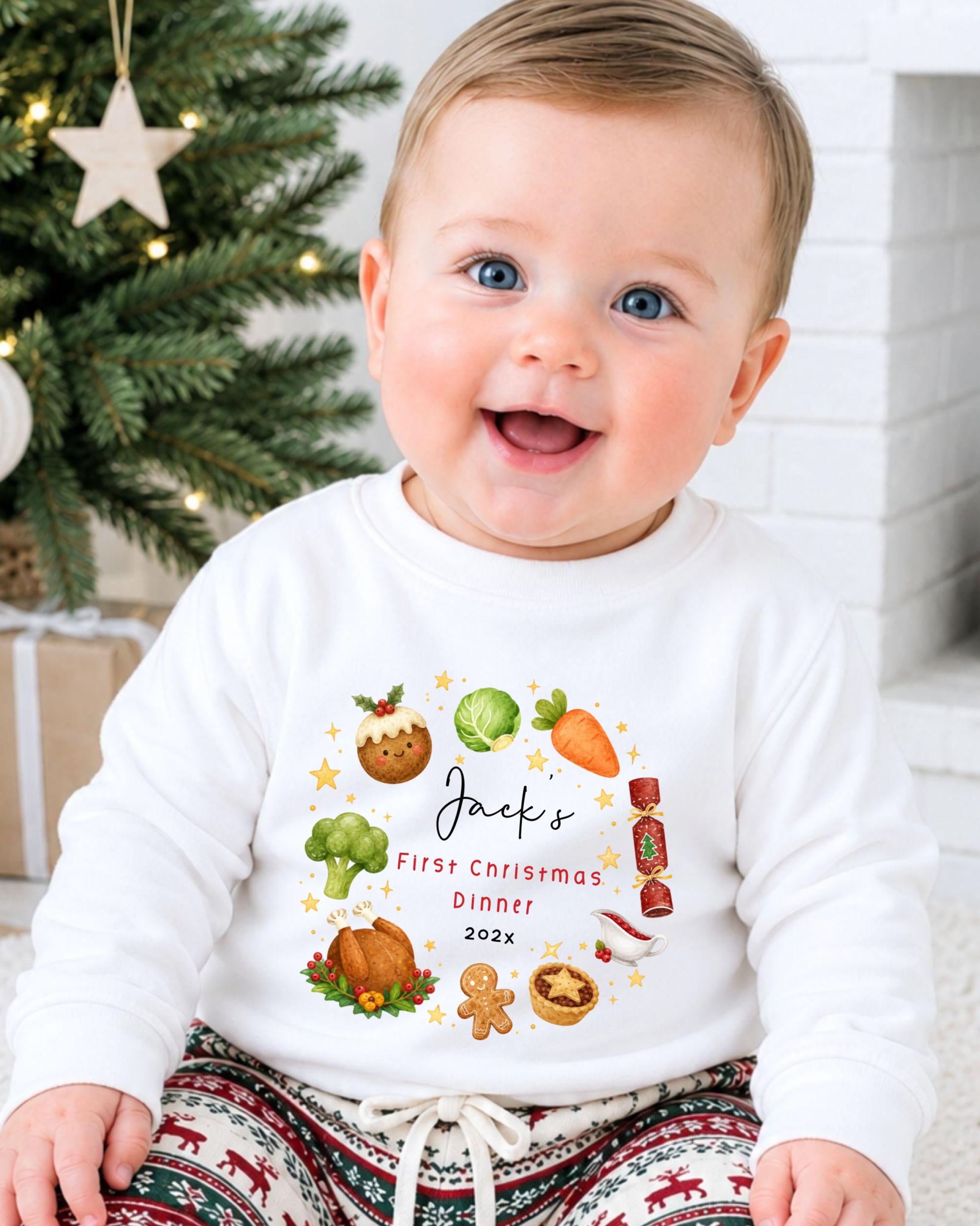 A smiling baby wearing a white shirt with a personalized Christmas-themed design, sitting in front of a Christmas tree.