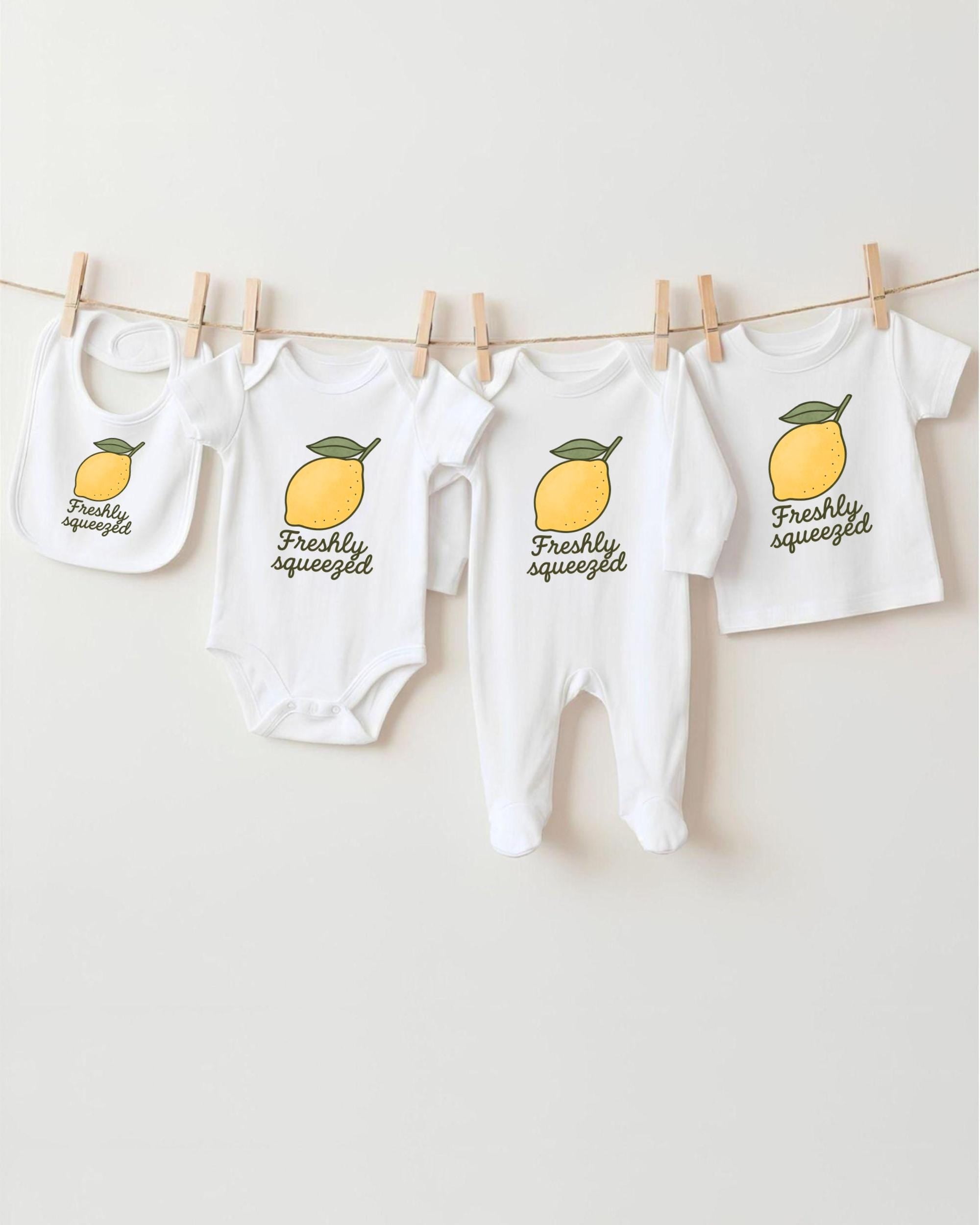 A collection of baby clothes, including onesies and bibs, hanging on a clothesline with a lemon graphic printed on them.