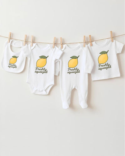 A collection of baby clothes, including onesies and bibs, hanging on a clothesline with a lemon graphic printed on them.