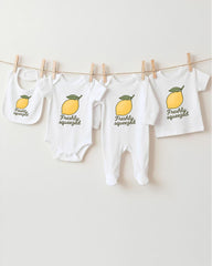 A collection of baby clothes, including onesies and bibs, hanging on a clothesline with a lemon graphic printed on them.