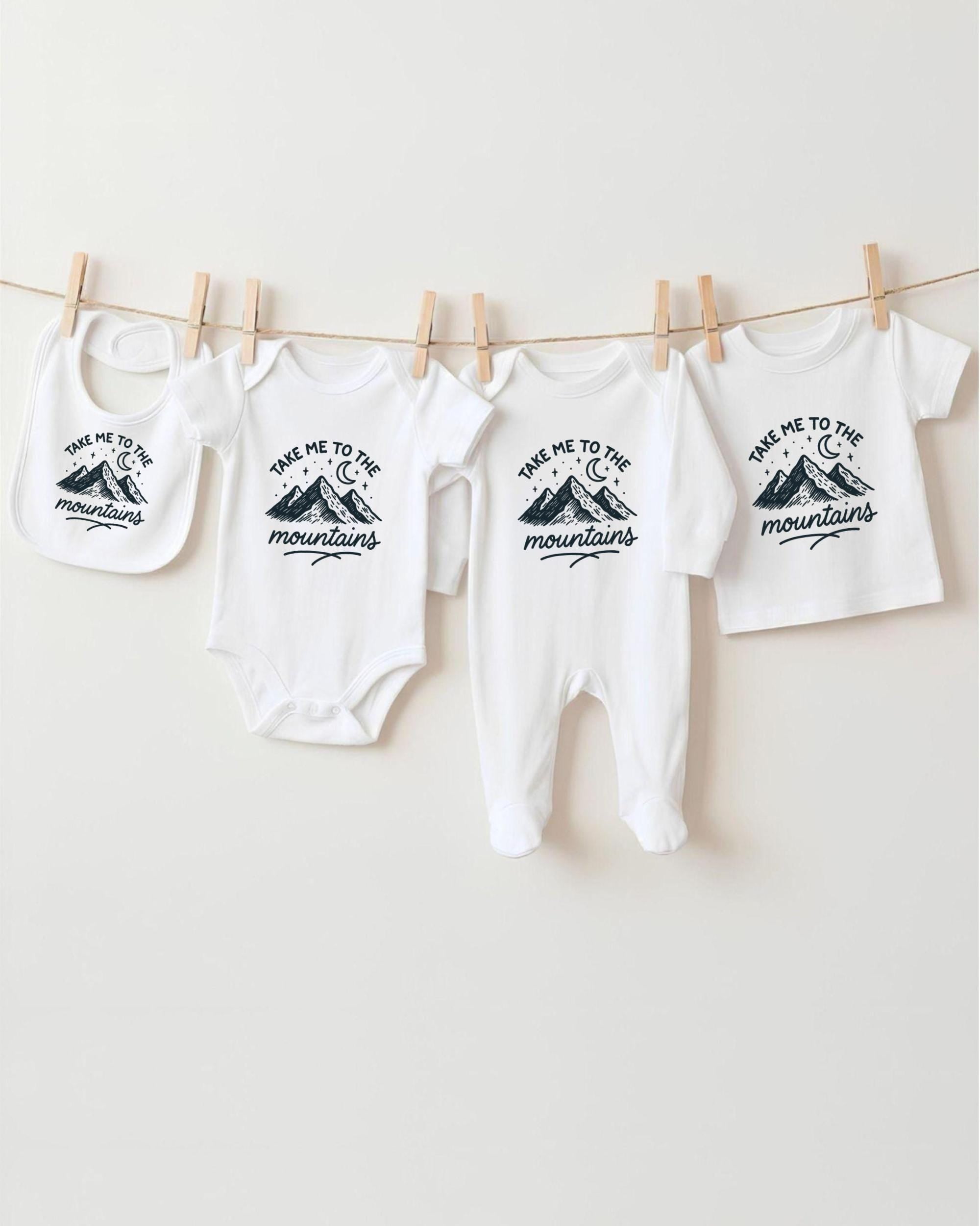 A row of four white baby clothes with mountain designs hanging on a clothesline.