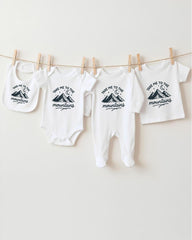 A row of four white baby clothes with mountain designs hanging on a clothesline.