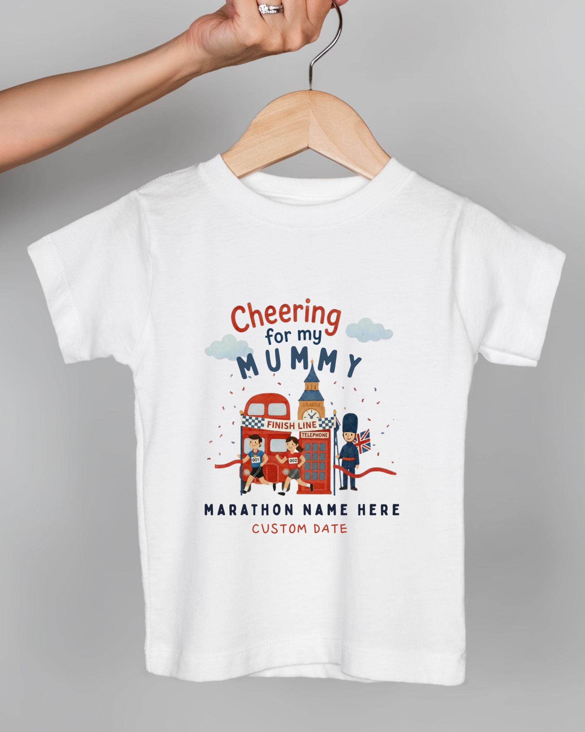 A white t-shirt with a graphic design depicting a person holding a sign that says "Cheering for my Mummy" and a red double-decker bus.
