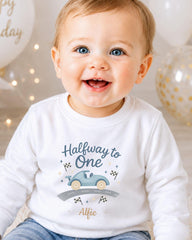 A smiling baby boy wearing a white shirt with a graphic of a car and the text "Halfway to One" and "Alfie" printed on it.