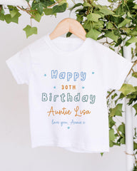 A white t-shirt with a birthday message printed on it, hanging on a wooden hanger.