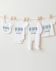 A collection of four white baby clothes, including onesies and pajamas, hanging on a clothesline.