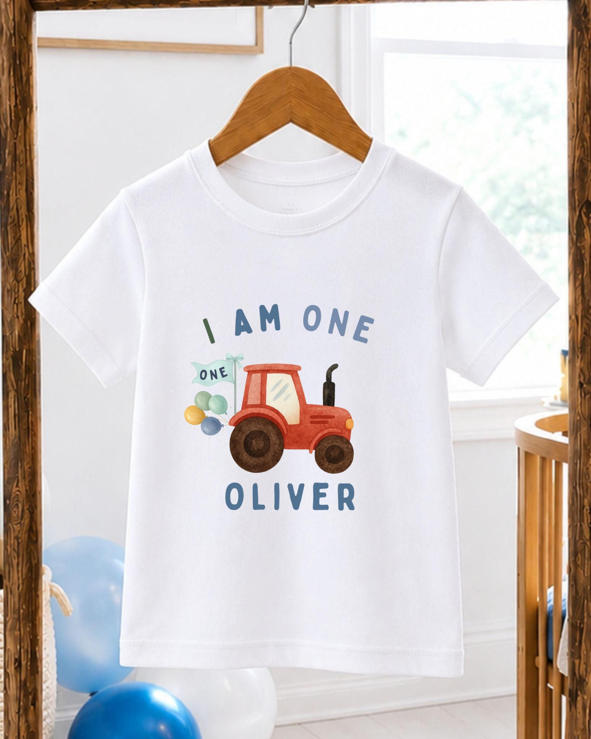 A white t-shirt with a graphic design of a red tractor and the text "I am one Oliver" printed on it.