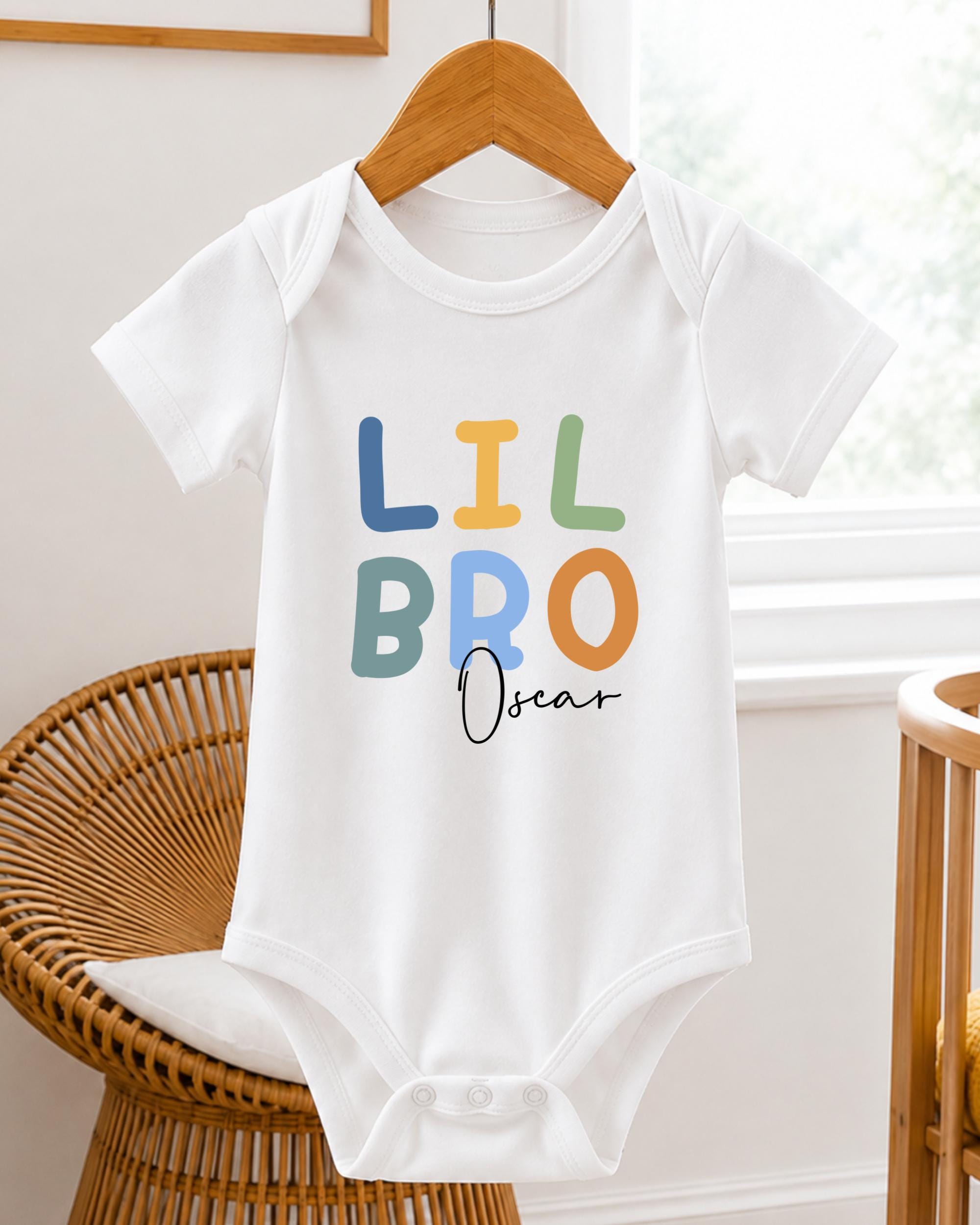 A white baby onesie with the text "LIL BRO Oscar" printed on it, hanging on a wooden hanger.