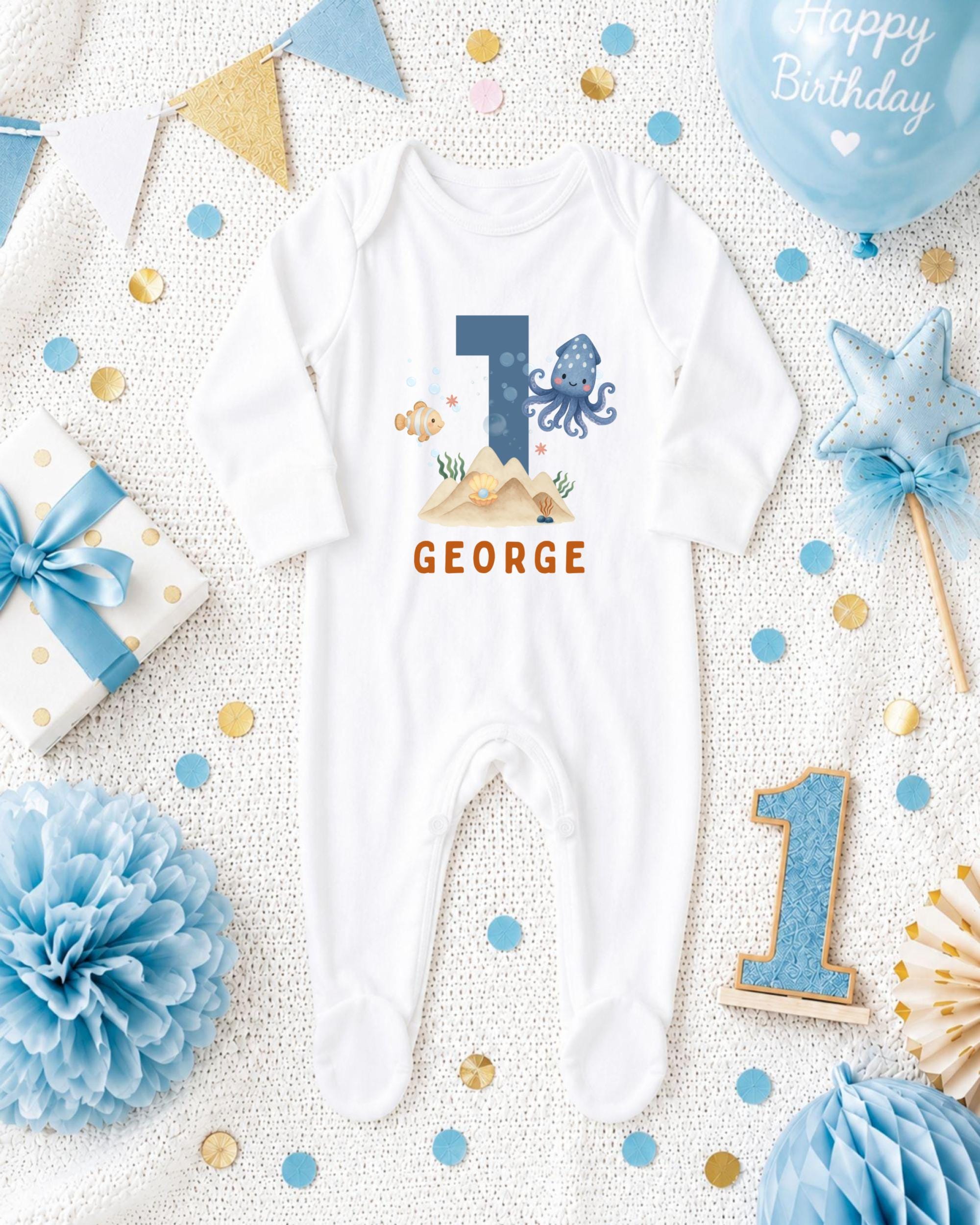 A white onesie with the number 1 and an octopus design, surrounded by birthday decorations such as a blue balloon, blue and gold confetti, and a blue and gold star.