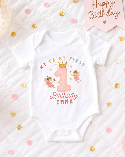 A white bodysuit with a birthday message and a fairy design, surrounded by confetti and a birthday card.