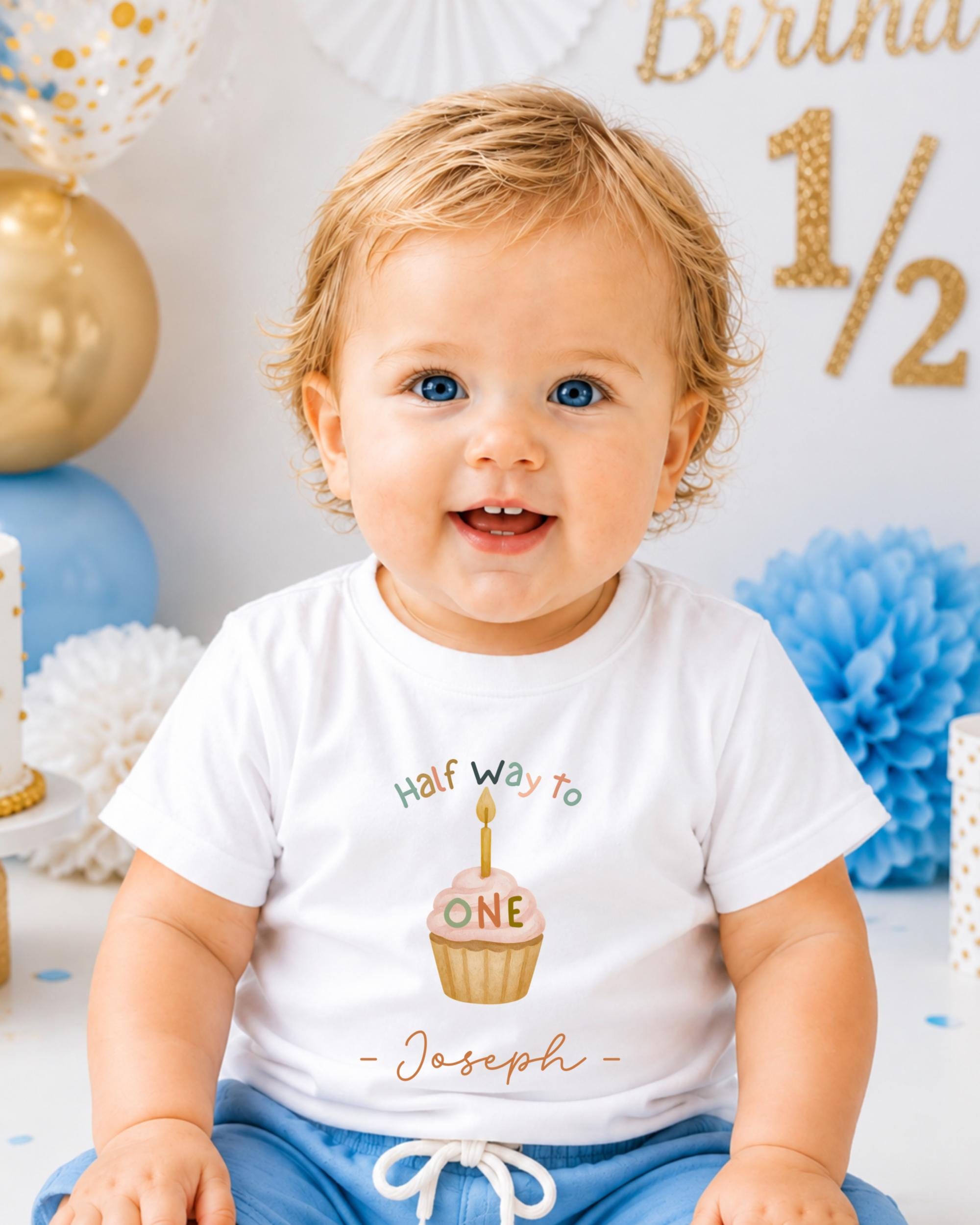 A smiling baby boy wearing a white t-shirt with a cupcake graphic and the text "Half way to Joseph" is sitting in front of a birthday party backdrop.
