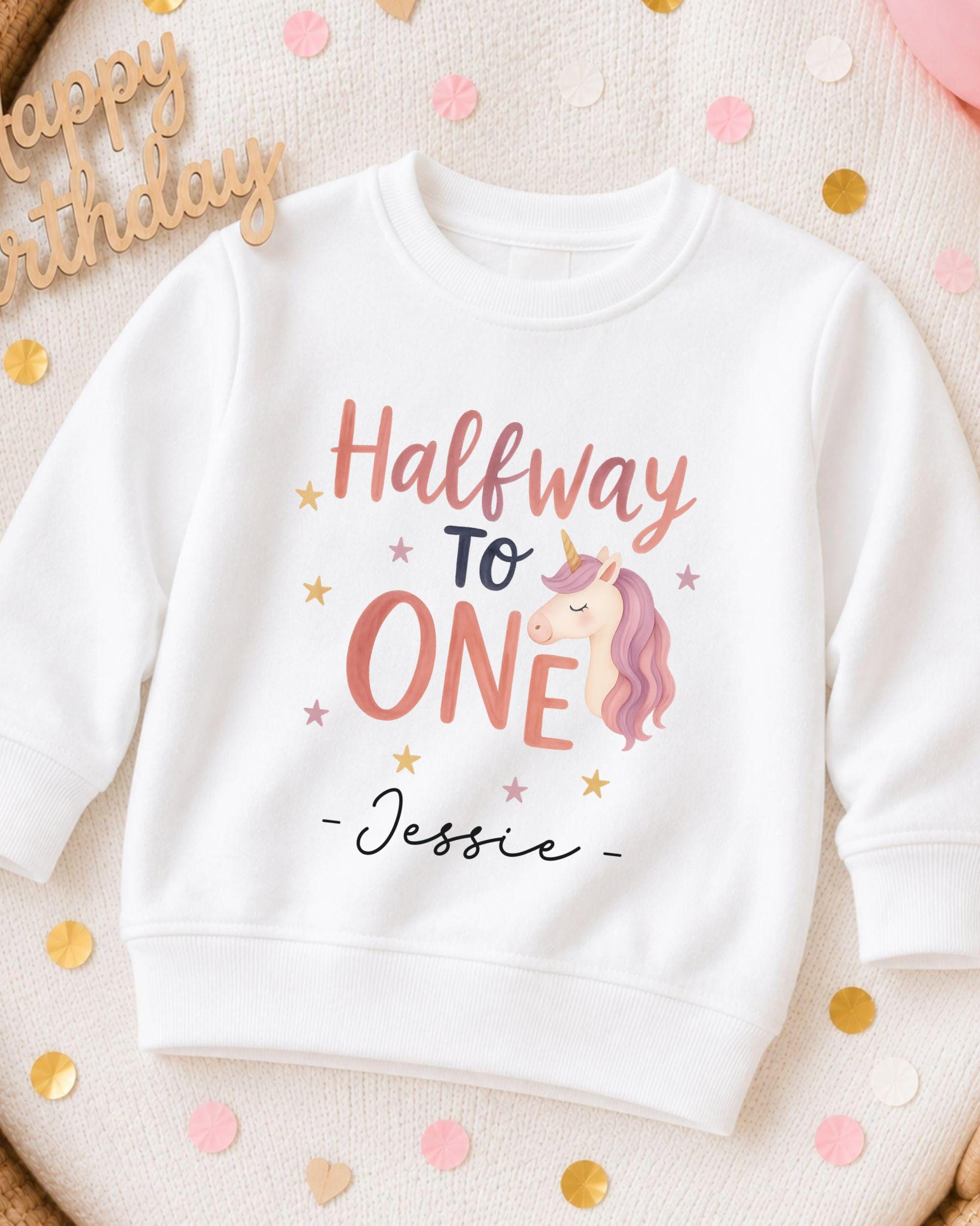 A white sweatshirt with a personalized text and a unicorn graphic printed on it, surrounded by confetti.