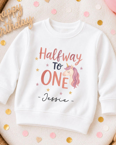 A white sweatshirt with a personalized text and a unicorn graphic printed on it, surrounded by confetti.