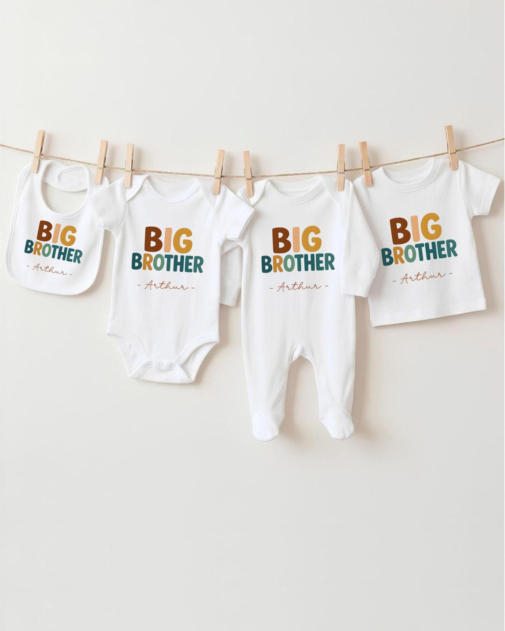 A row of four white baby clothes with the text "BIG BROTHER" printed on them, hanging on a clothesline.
