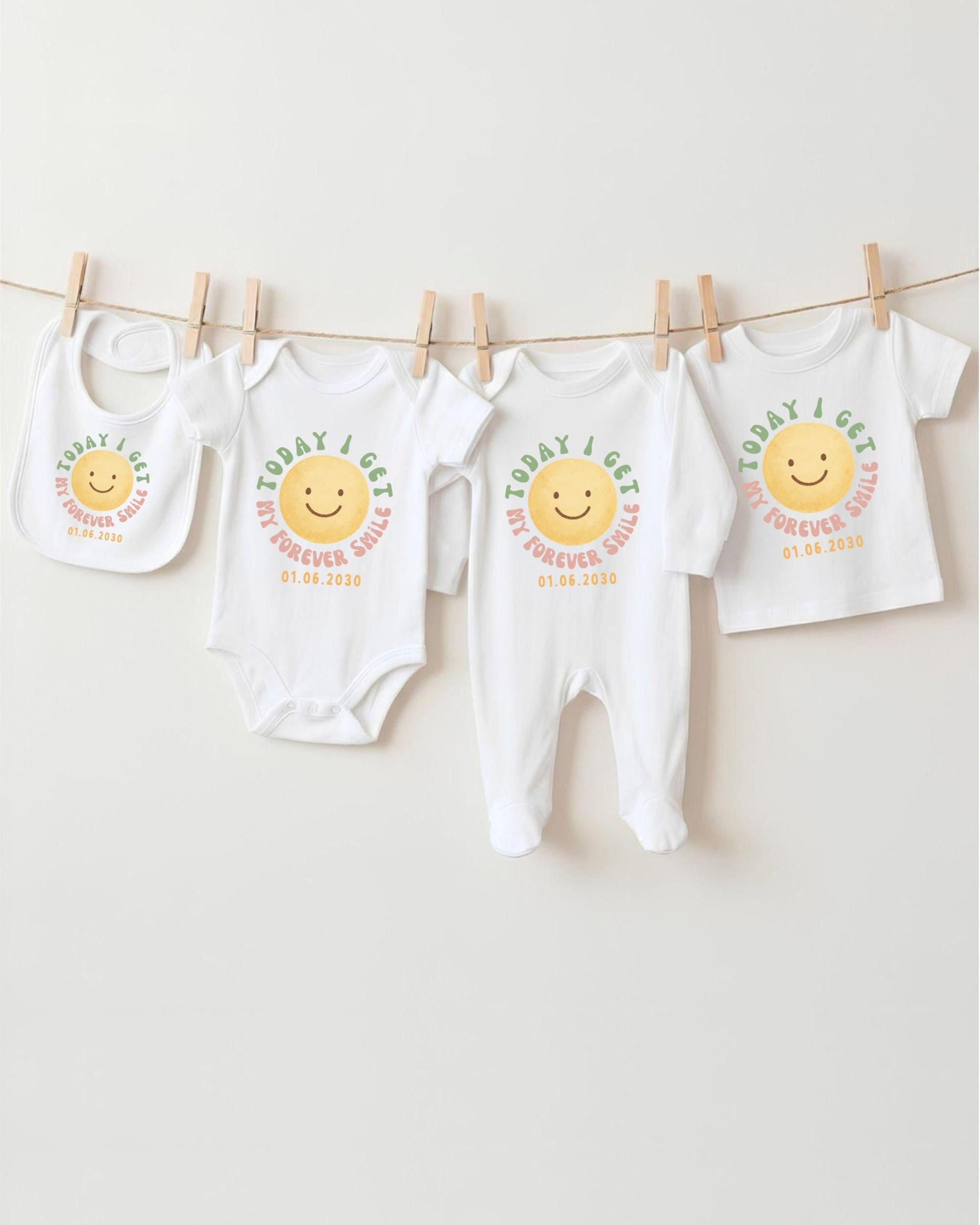A row of four white baby clothes with a smiley face design, hanging on a clothesline.
