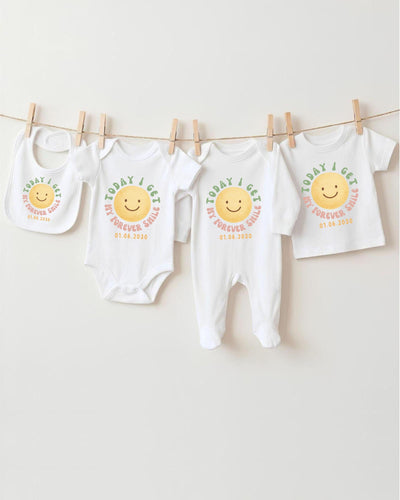 A row of four white baby clothes with a smiley face design, hanging on a clothesline.