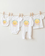 A row of four white baby clothes with a smiley face design, hanging on a clothesline.